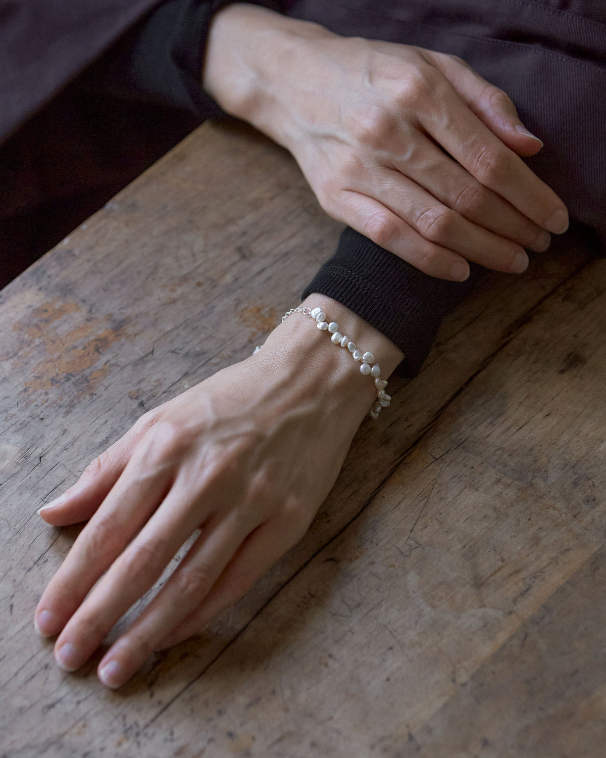 A person's wrist wearing a silver oval belcher chain bracelet with white keshi and baroque freshwater pearls.