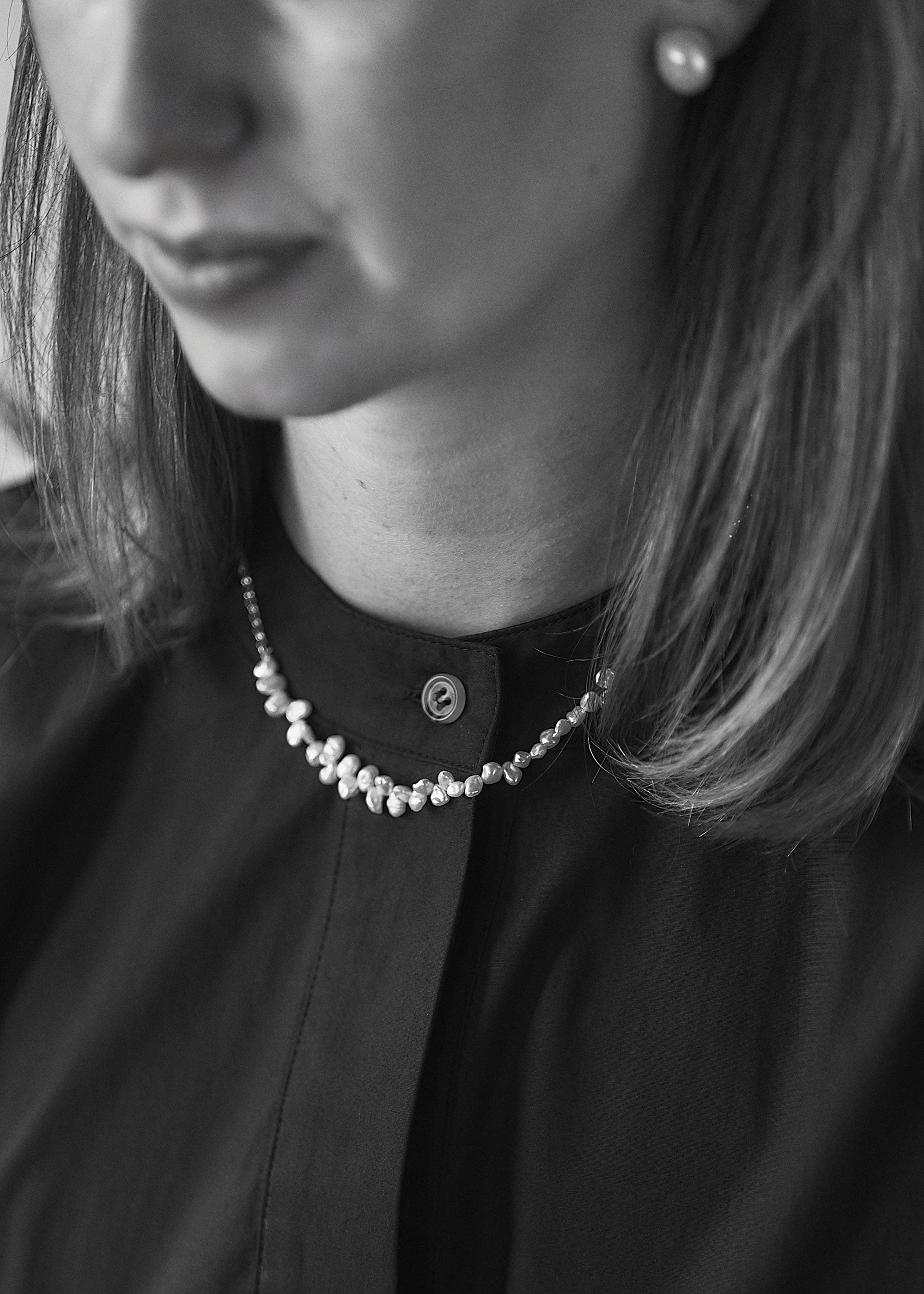 Close-up of a person wearing a necklace with a black shirt and pearl earring.