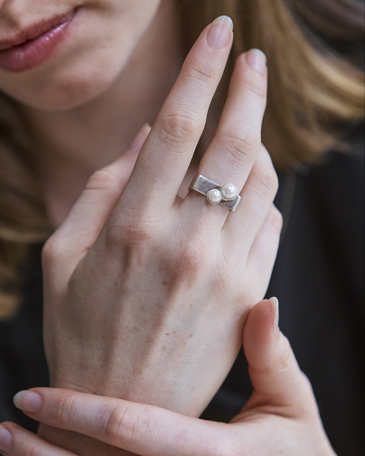 A close-up image of a person's hand showcasing a sterling silver ring with two freshwater pearls.