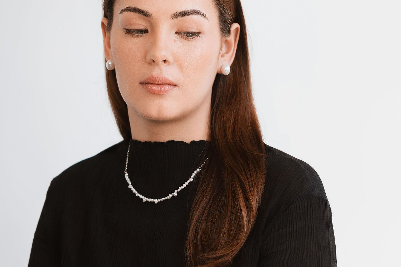 Woman wearing a black top and pearl necklace against a light gray background