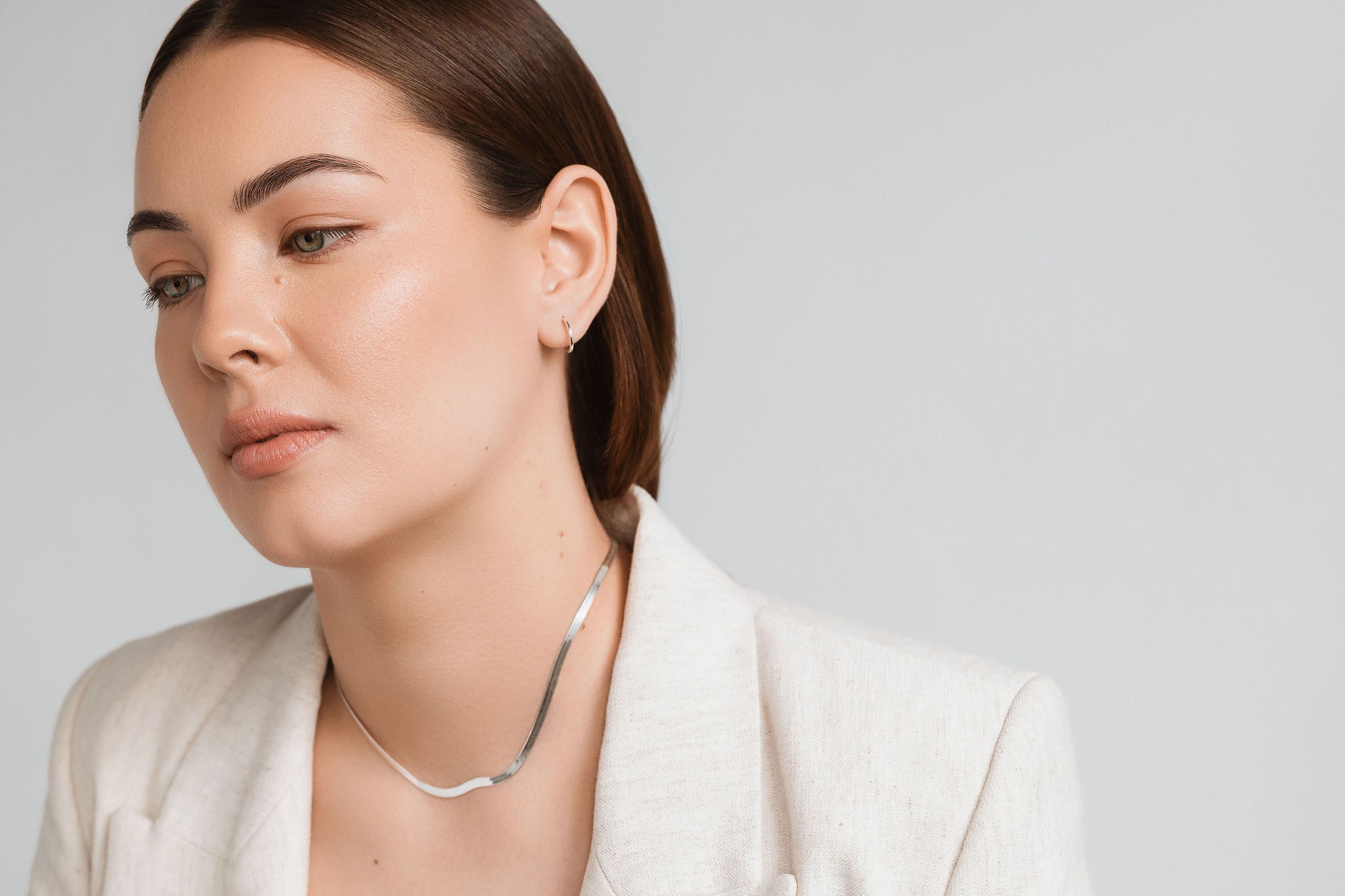 Woman wearing a silver necklace and earring on a plain background