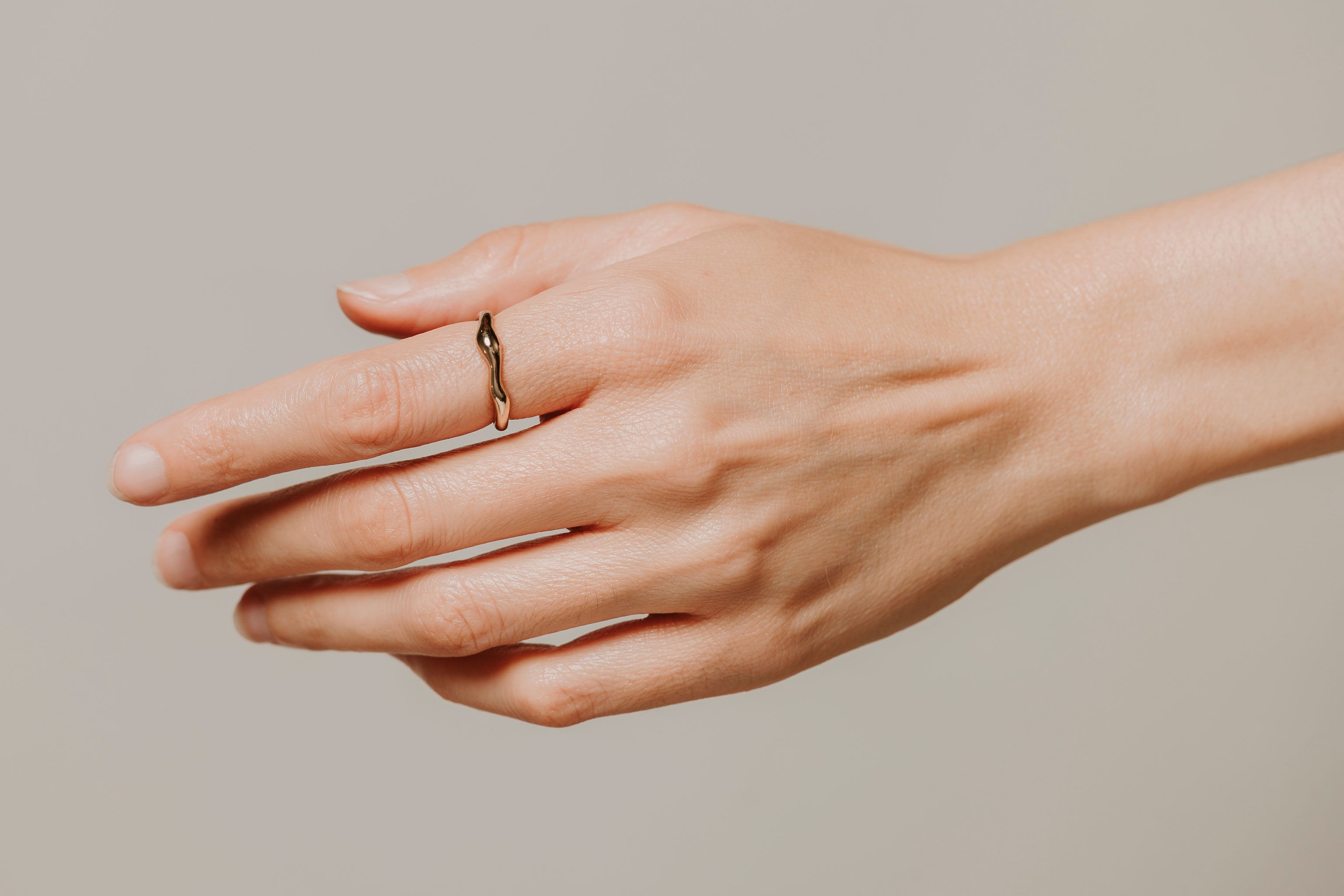 Hand wearing a gold ring on a neutral background