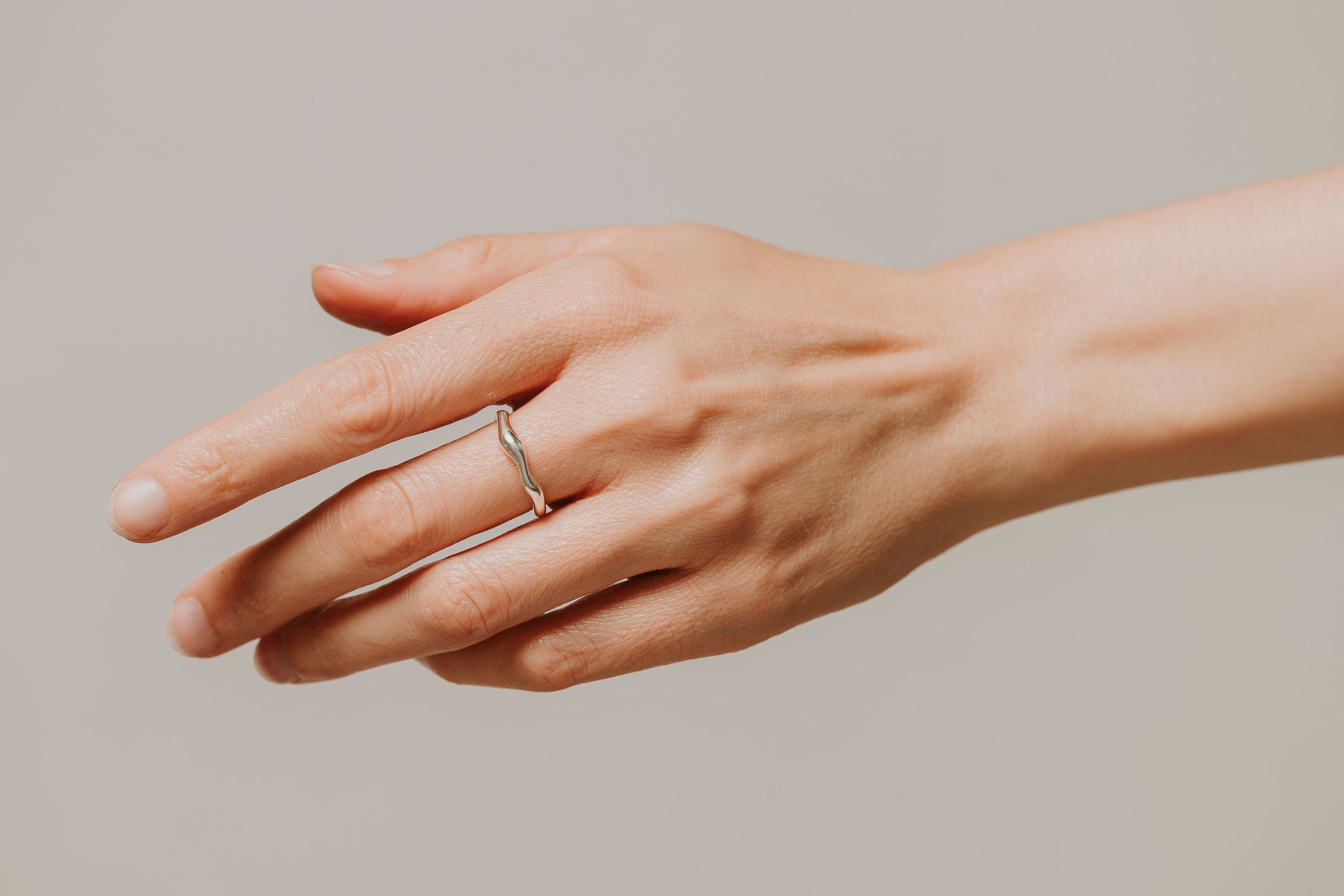 Hand wearing a silver ring on a plain background