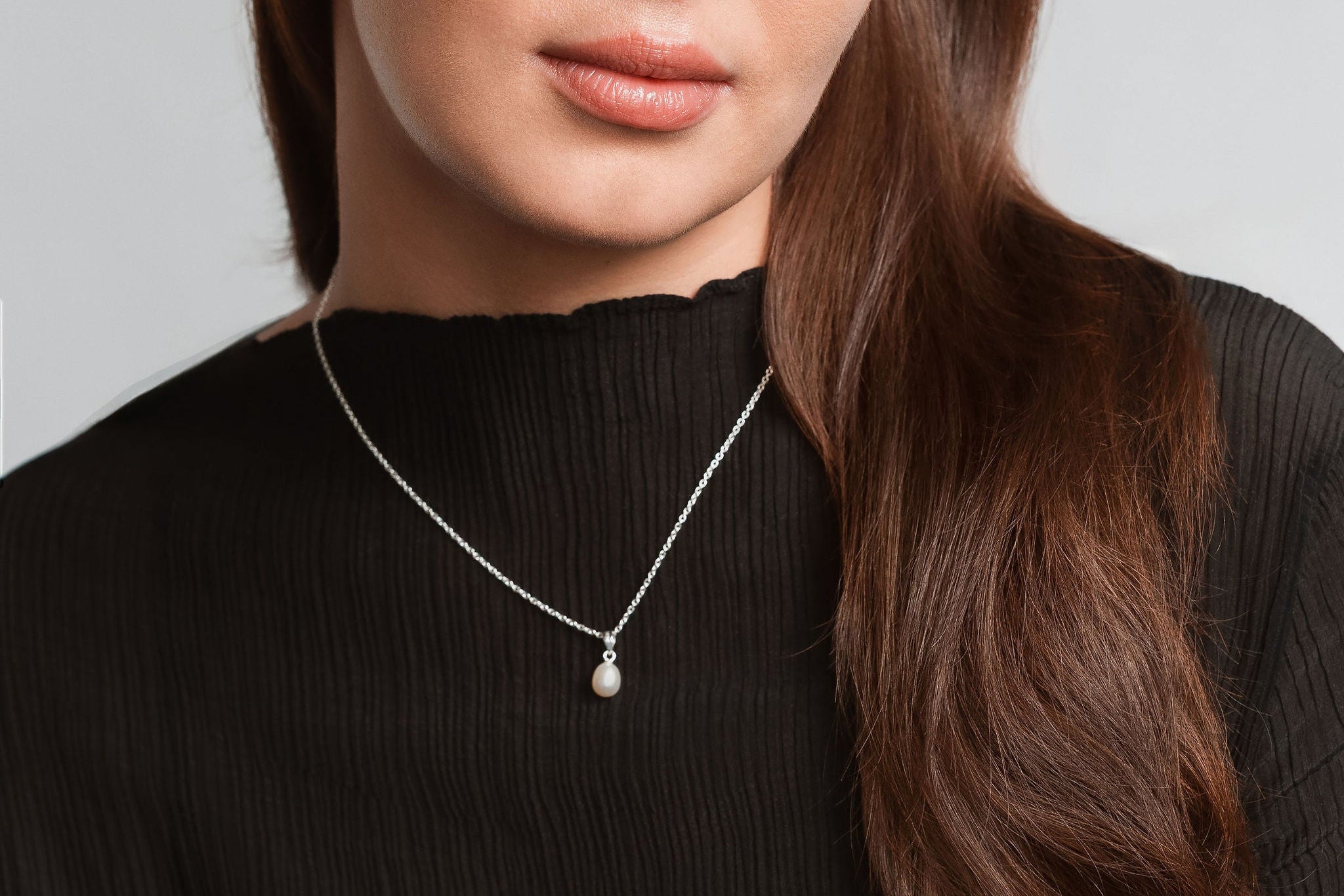 Woman wearing a black top and necklace against a plain background