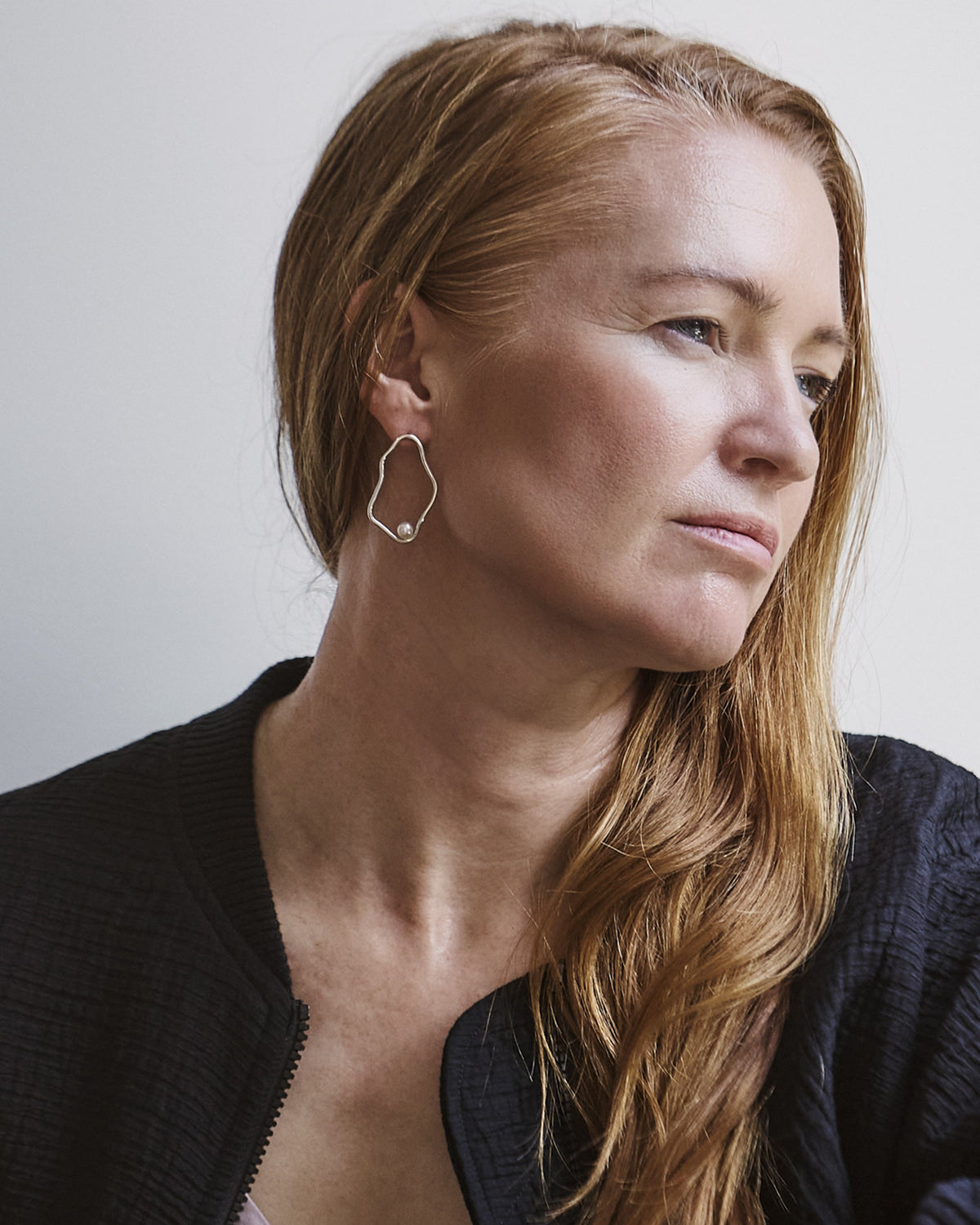 A person wearing the Mariana Earrings, which are silver stud earrings with freshwater pearls.