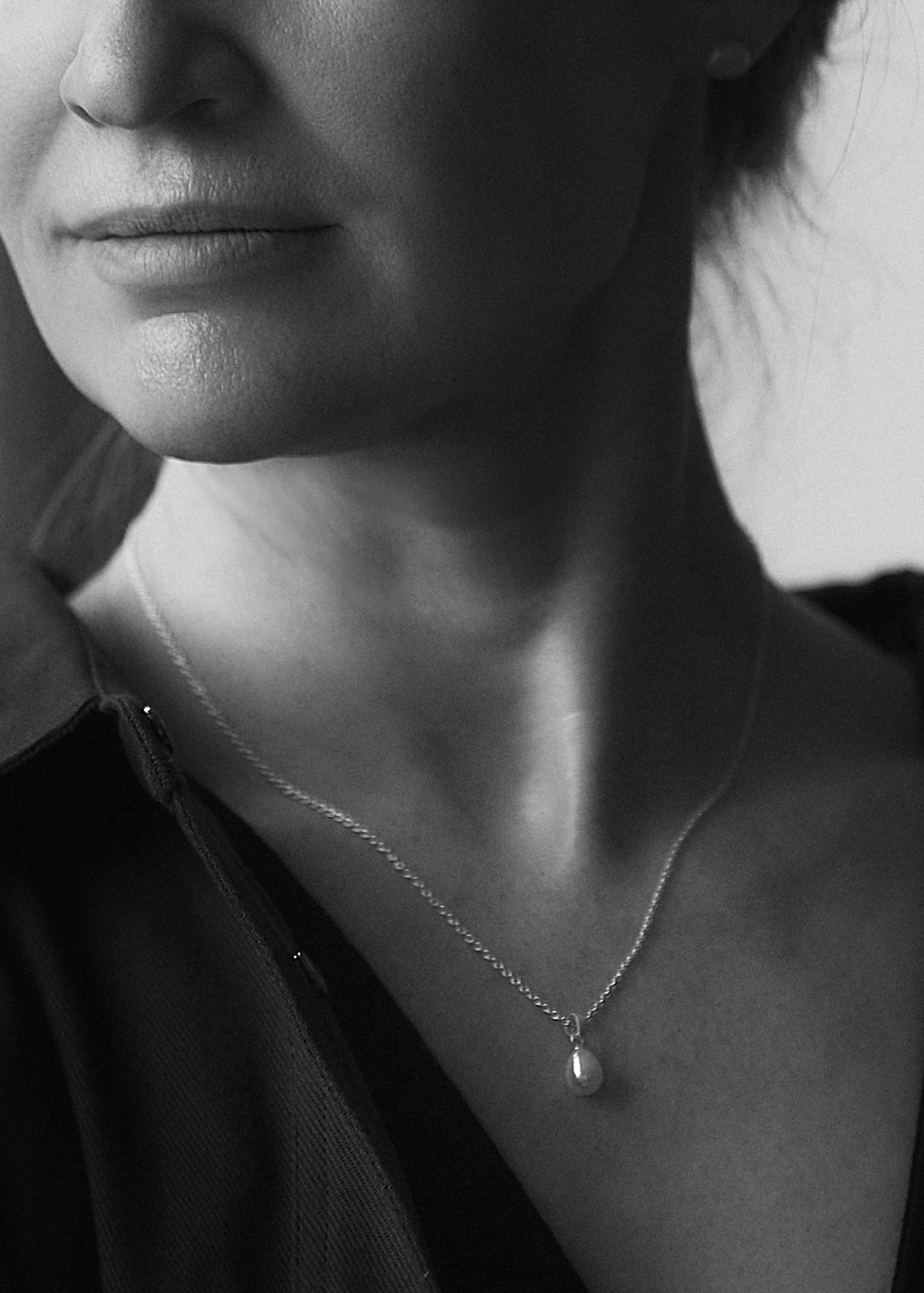 A black and white image of a person wearing a sterling silver cable chain pendant necklace with a lustrous pearl drop.