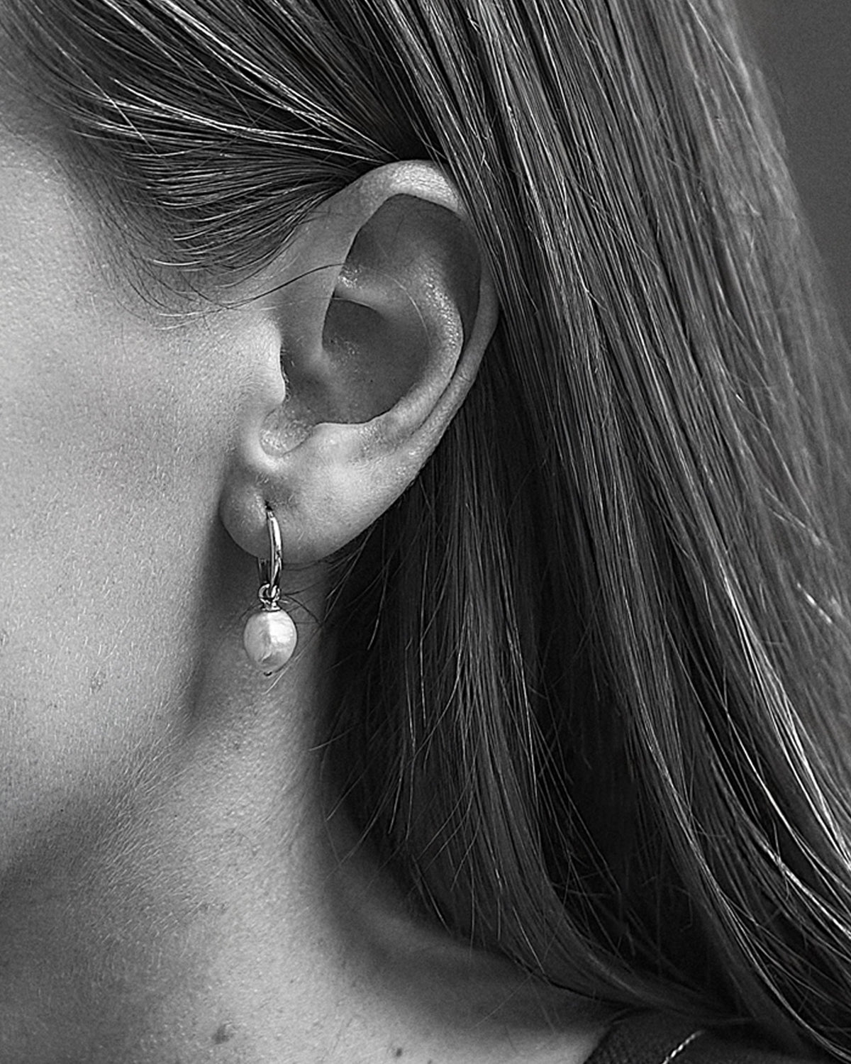 A black and white image of a person wearing a hoop earring with a pearl detail.