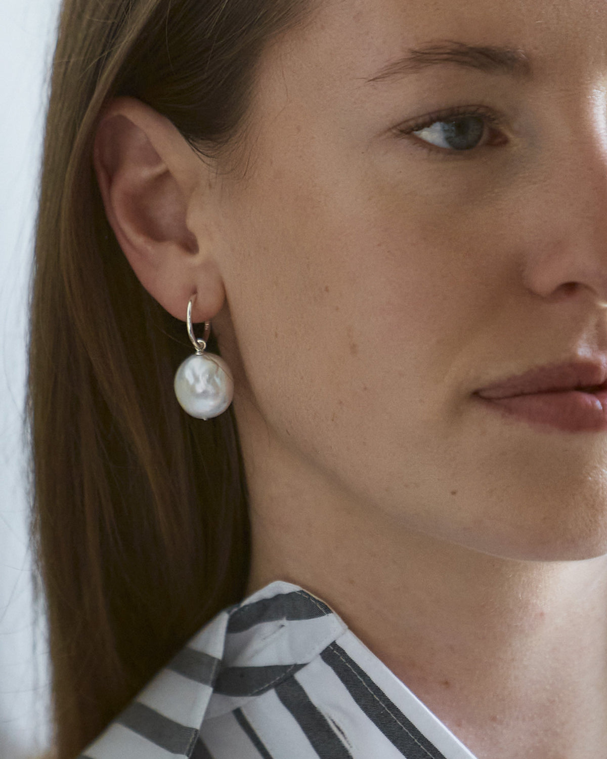 A close-up image of a woman's face, focusing on a hoop earring with a baroque freshwater pearl