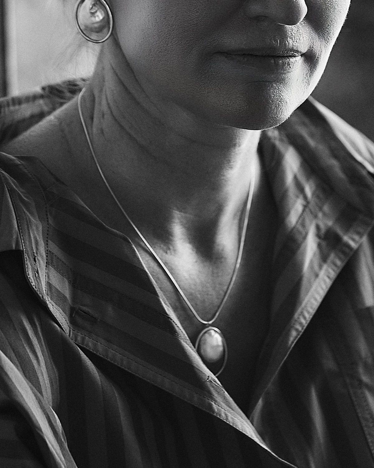 A close-up black and white image of a sterling silver necklace with a freshwater pearl pendant, worn by a person.
