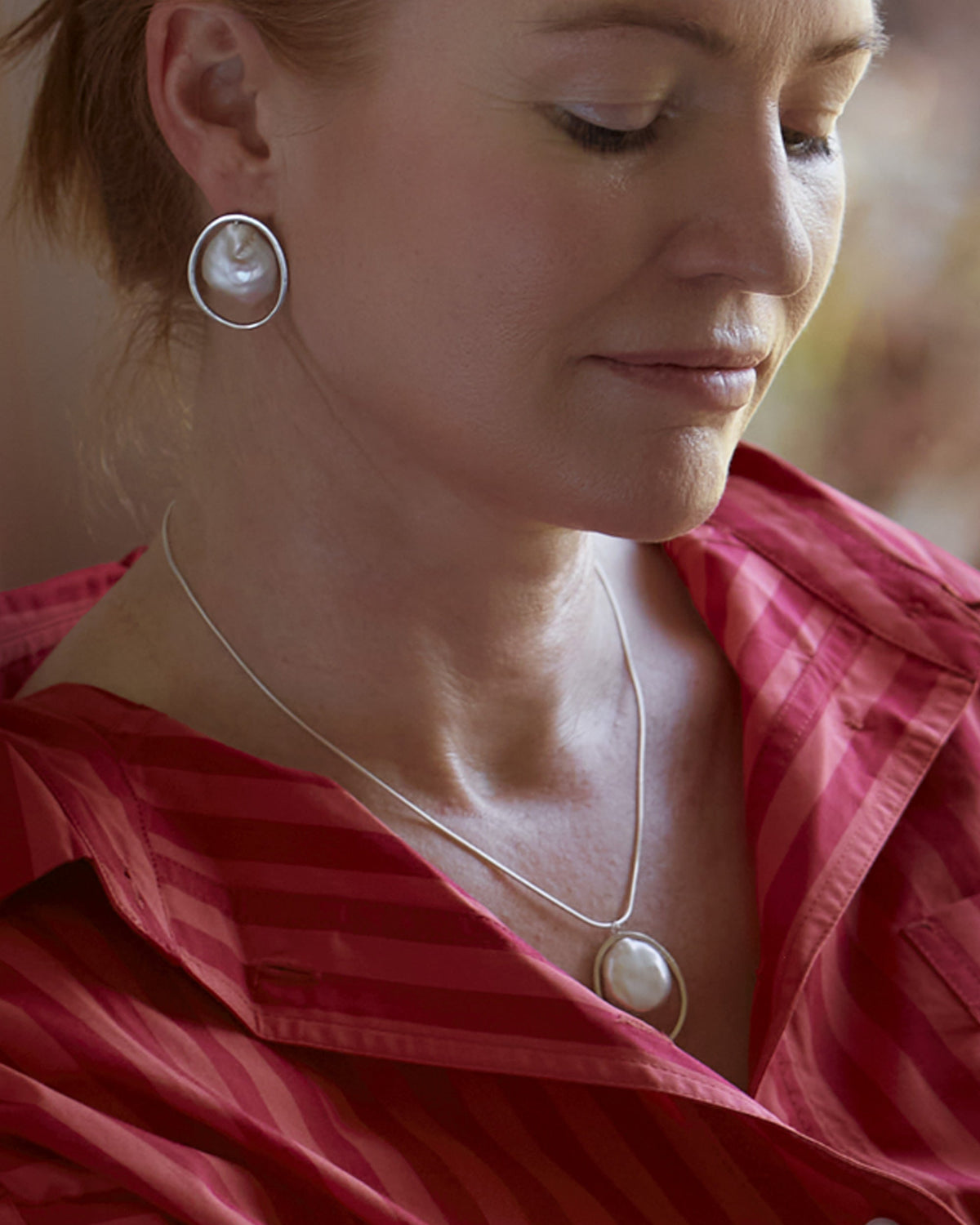 A person wearing a red shirt, featuring a sterling silver necklace with a freshwater pearl pendant.
