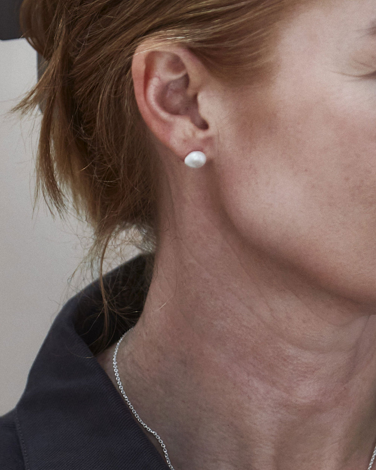 A close-up image of a person's ear wearing a silver stud earring with a white keshi freshwater pearl.
