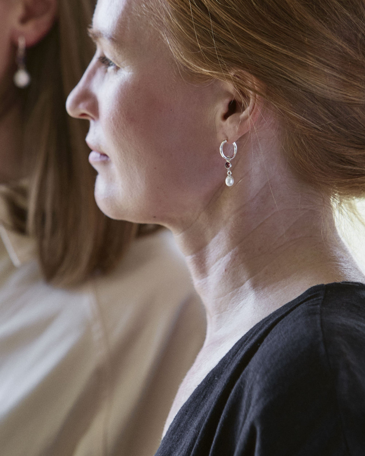 A person viewed from the side wearing drop-shaped freshwater pearl earrings with rose-cut pink tourmaline suspended from smooth hoops.