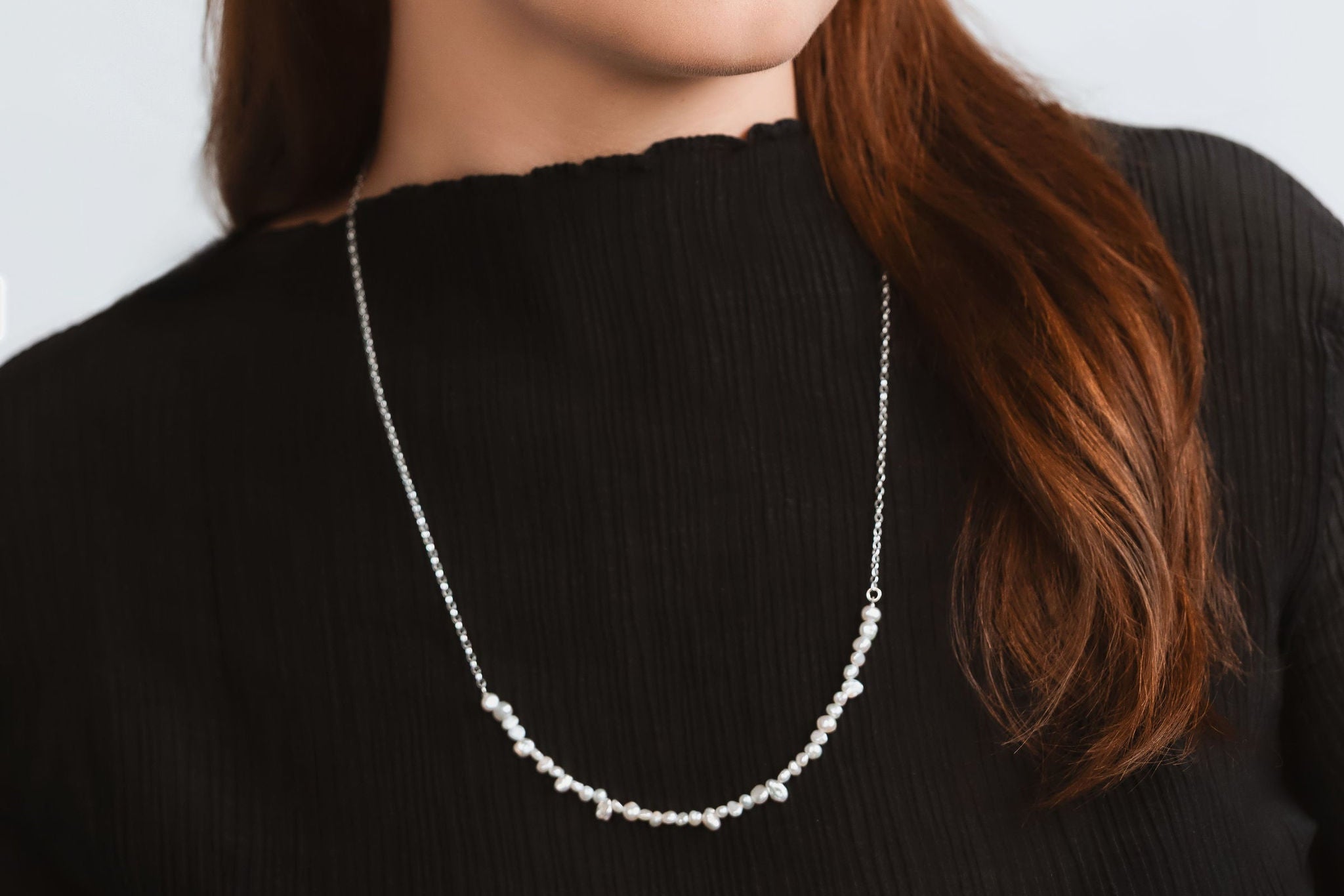 Woman wearing a pearl and silver necklace against a plain background