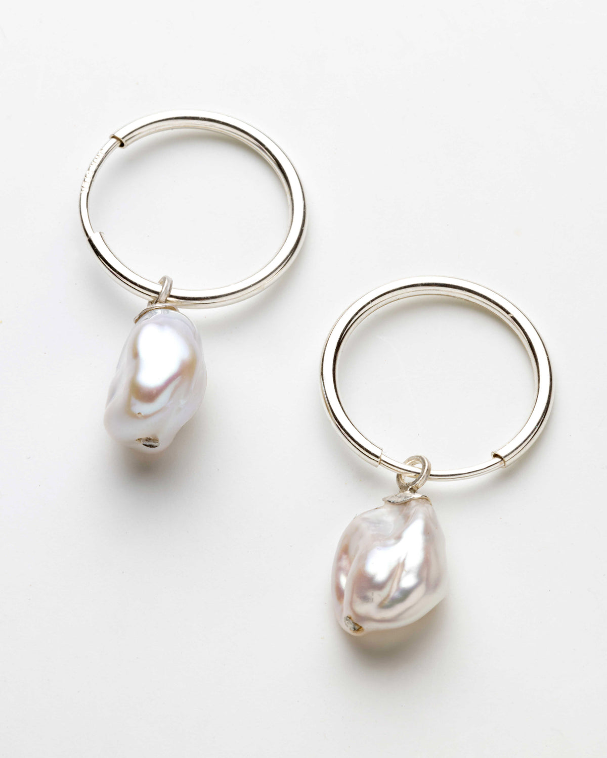 A pair of silver hoop earrings with irregular white baroque pearls dangling from the bottom of each hoop, photographed on a clean white background.